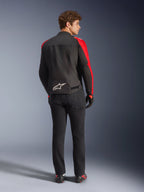 Veste imperméable Alpinestars T-SPS V2, noir, rouge et rouge fluo, vue de dos sur un modèle masculin, logo Alpinestars blanc en bas du dos, portée avec un pantalon de moto noir et des gants, veste de moto en textile imperméable au style sportif