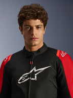 Modèle masculin portant la veste imperméable Alpinestars T-SPS V2, noire avec accents rouges et logo blanc, portrait en gros plan, veste de moto de sport en textile