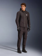 Modèle masculin portant la veste imperméable Alpinestars Aeroshell WP noire, design à capuche softshell avec fermeture éclair imperméable et logo ASTARS blanc sur la poitrine, assortie d'un pantalon de moto, de gants et de bottes noirs, style de conduite sport-naked moderne.