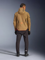 Veste Alpinestars Aeroshell Waterproof en Kaki Foncé Noir Orange Fluo, vue de dos d'un homme portant la veste softshell à capuche, avec liserés noirs et logo orange, associée à un pantalon technique noir et des gants.