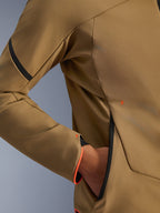 Gros plan sur la veste imperméable Alpinestars Aeroshell WP, kaki foncé avec accents noir et orange fluo, détails de la poche zippée invisible et du poignet, textile softshell extensible pour la conduite à moto