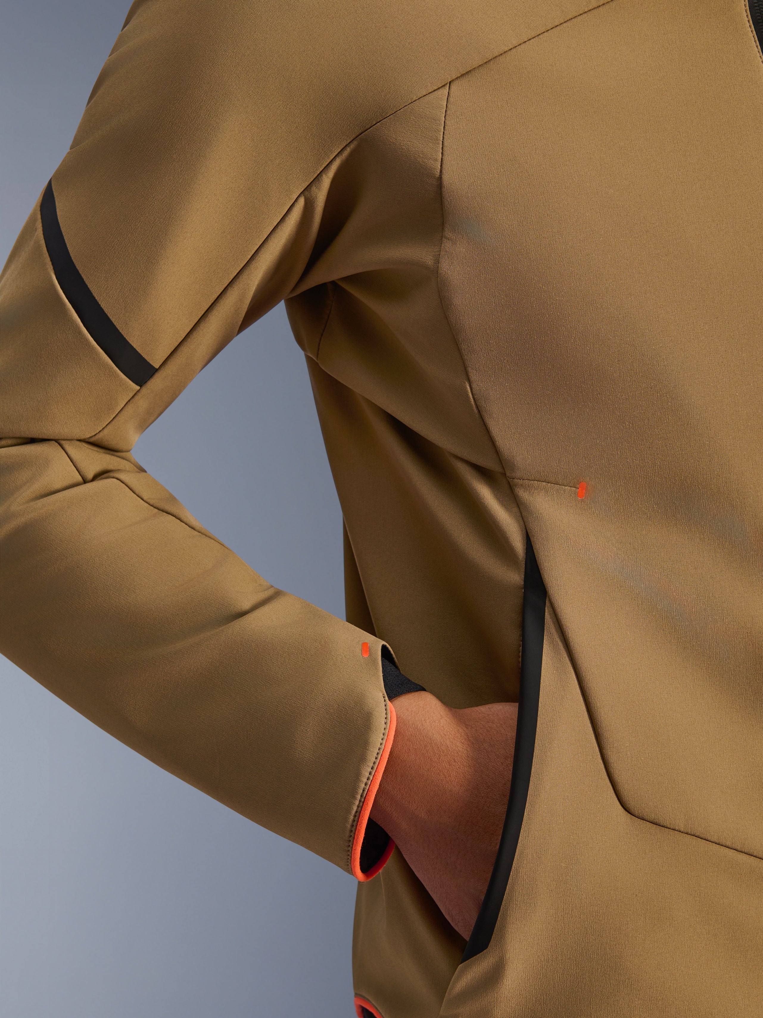 Gros plan sur la veste imperméable Alpinestars Aeroshell WP, kaki foncé avec accents noir et orange fluo, détails de la poche zippée invisible et du poignet, textile softshell extensible pour la conduite à moto
