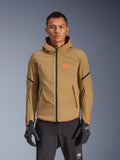 Alpinestars Aeroshell Waterproof Jacket, veste de moto à capuche kaki foncé avec logos orange et fermetures éclair noires, lignes d'accent noires sur les manches, portée avec des gants et un pantalon noirs