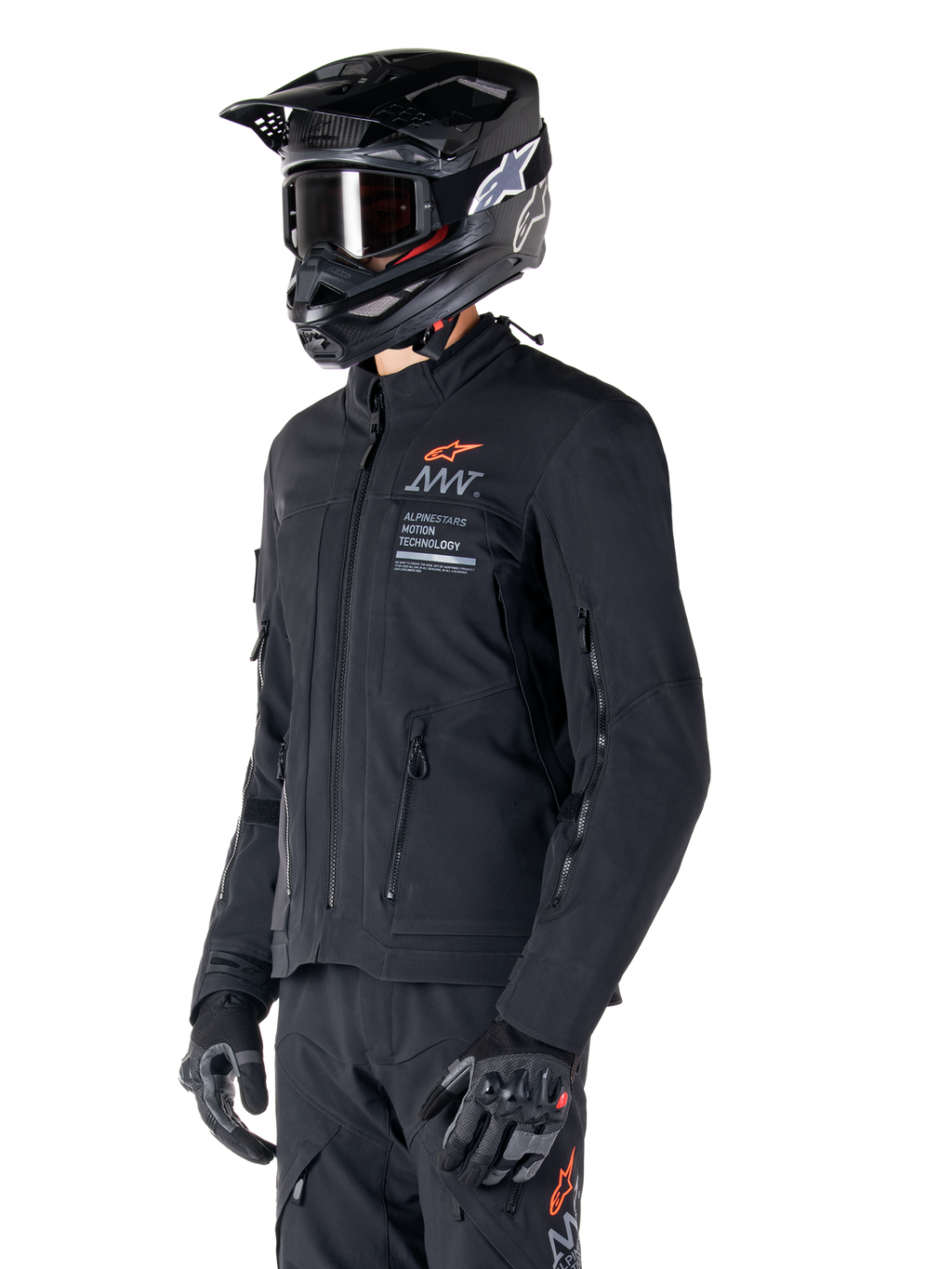 Veste Alpinestars AMT-8 Stretch Drystar® XF, noire, portée par un pilote avec pantalon d'aventure et gants assortis, comprenant un casque de motocross noir et des lunettes, ouvertures de ventilation zippées sur la poitrine et les bras, marquage Alpinestars Motion Technology avec logo orange, équipement d'aventure-touring haut de gamme