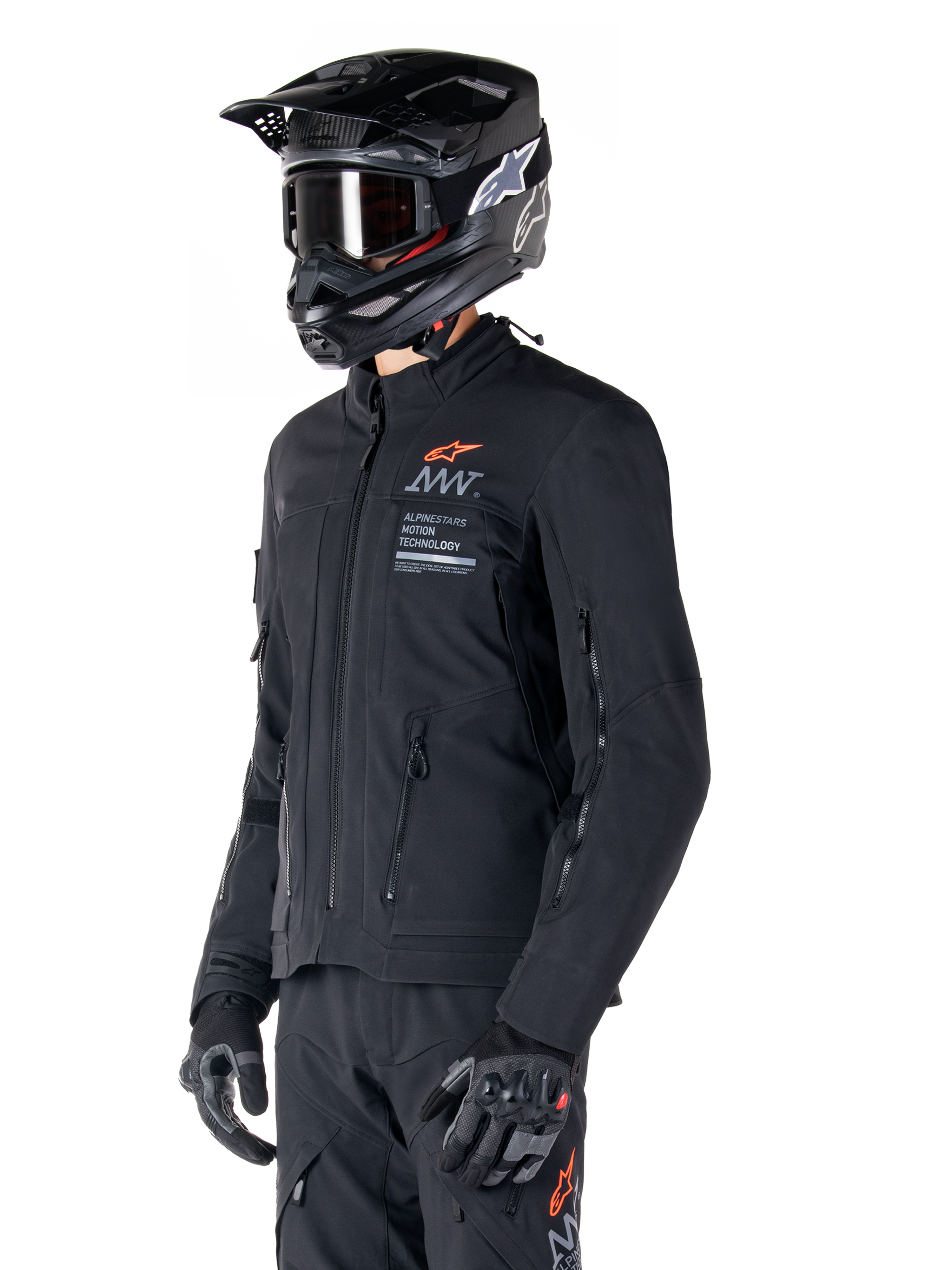 Veste Alpinestars AMT-8 Stretch Drystar® XF, noire, portée par un pilote avec pantalon d'aventure et gants assortis, comprenant un casque de motocross noir et des lunettes, ouvertures de ventilation zippées sur la poitrine et les bras, marquage Alpinestars Motion Technology avec logo orange, équipement d'aventure-touring haut de gamme