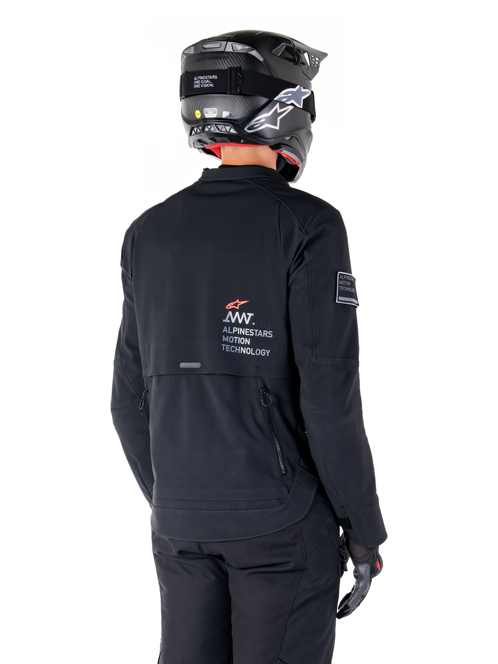 Vue arrière d'un pilote portant la veste Alpinestars AMT-8 Stretch Drystar® XF noire, avec le logo « AMT Alpinestars Motion Technology » dans le dos, des ventilations techniques zippées, assortie d'un casque de moto et de gants noirs