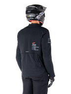 Vue arrière d'un pilote portant la veste Alpinestars AMT-8 Stretch Drystar® XF noire, avec le logo « AMT Alpinestars Motion Technology » dans le dos, des ventilations techniques zippées, assortie d'un casque de moto et de gants noirs