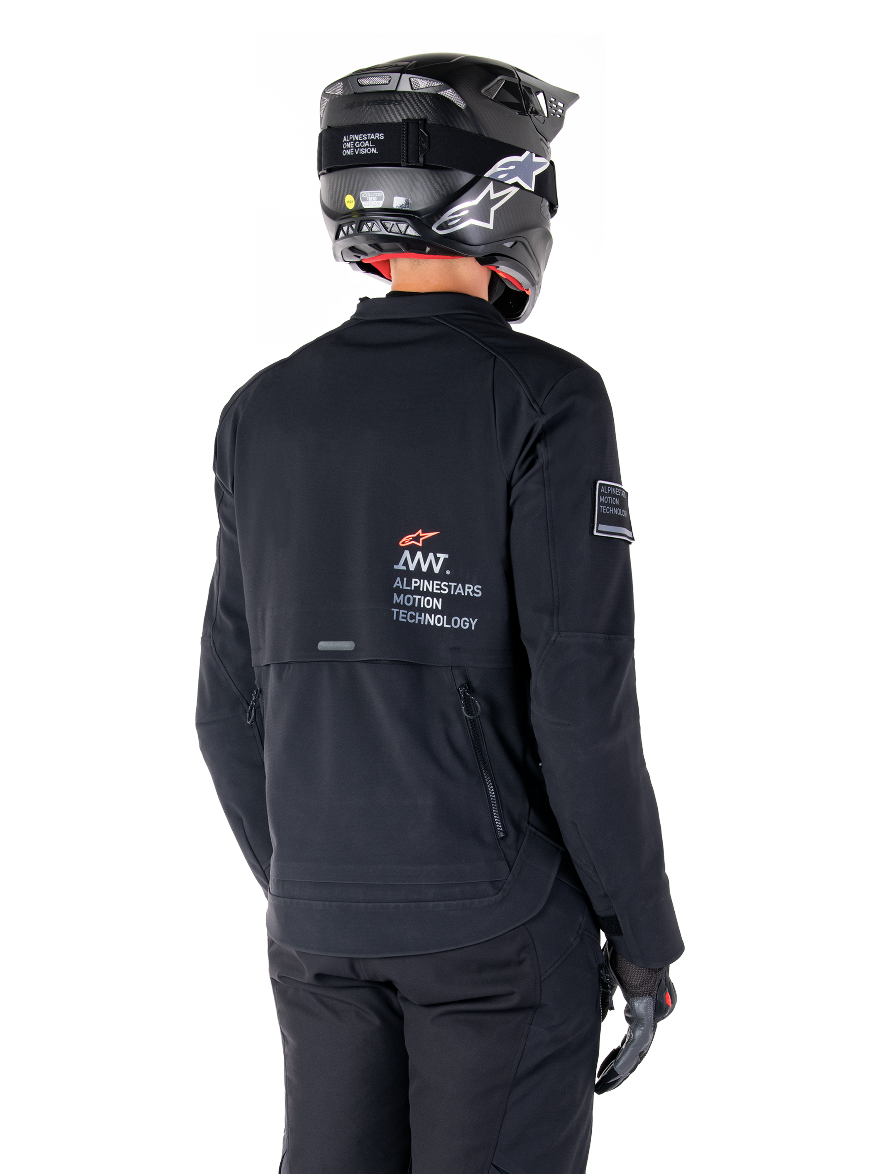 Vue arrière d'un pilote portant la veste Alpinestars AMT-8 Stretch Drystar® XF noire, avec le logo « AMT Alpinestars Motion Technology » dans le dos, des ventilations techniques zippées, assortie d'un casque de moto et de gants noirs
