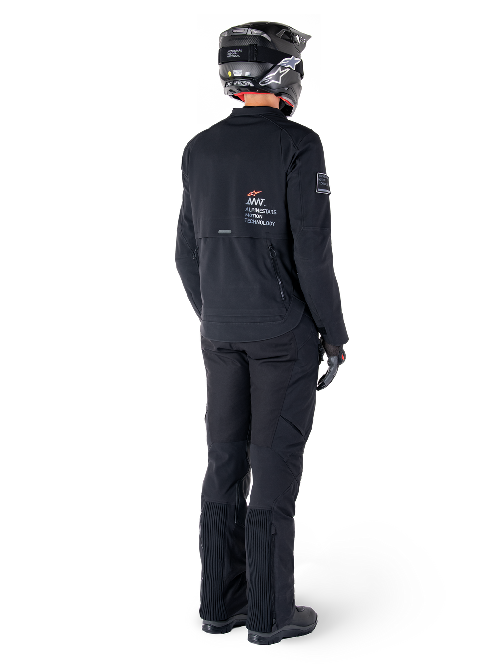 Veste Alpinestars AMT-8 Stretch Drystar® XF, noire, vue arrière d'un pilote portant la veste avec un pantalon noir assorti et un casque noir, arborant le marquage « Alpinestars Motion Technology » dans le dos, matériau stretch technique pour la pratique de la moto d'aventure