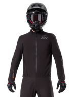 Doublure Alpinestars AMT-8 Stretch Drystar® XF, doublure de moto imperméable noire, dotée d'une fermeture éclair frontale et d'une taille élastiquée, logo AMT sur la poitrine et marquage Drystar XF sur la manche, portée avec un casque et des gants noirs.