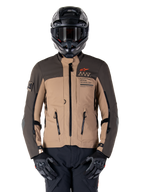 Veste Alpinestars AMT-8 Stretch Drystar XF, veste de moto d'aventure touring, kaki foncé et marron foncé, avec logo Astars orange et fermetures éclair noires, portée avec un casque d'aventure noir et des gants noirs, tenue de moto complète