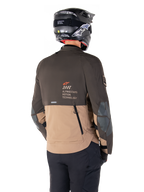 Veste Alpinestars AMT-8 Stretch Drystar® XF, veste de moto d'aventure, brun foncé et kaki foncé, vue arrière montrant le marquage AMT Alpinestars Motion Technology, design textile bicolore avec fermetures éclair de ventilation à l'arrière et échappement en bardeaux, portée avec un casque noir et un pantalon de moto