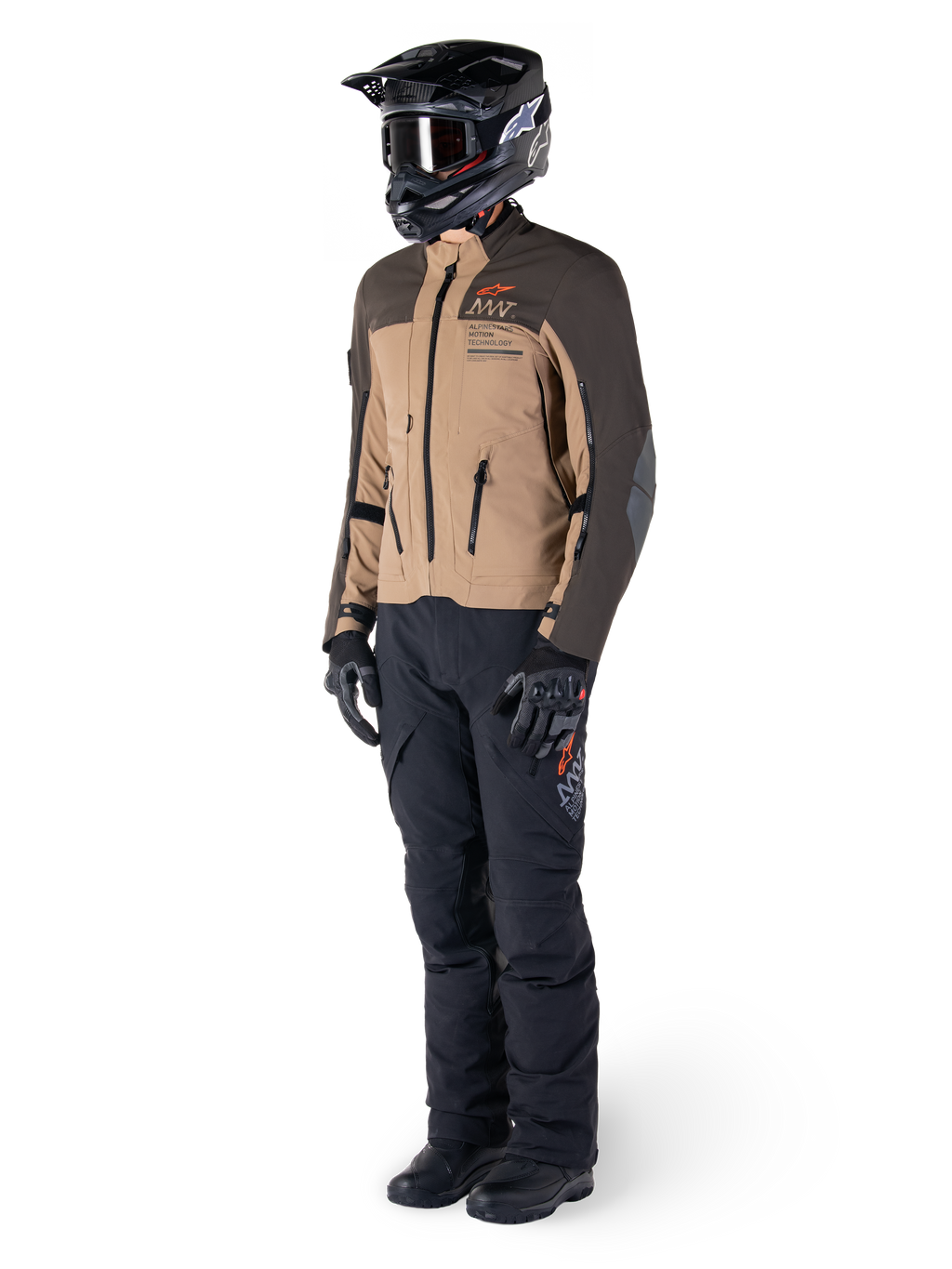 Pilote d'aventure portant un équipement complet, veste Alpinestars AMT-8 Stretch Drystar® XF en brun foncé et kaki foncé, associée à un pantalon d'aventure noir, un casque, des gants et des bottes noirs, avec logo AMT orange et fermetures éclair de ventilation techniques pour le touring longue distance.