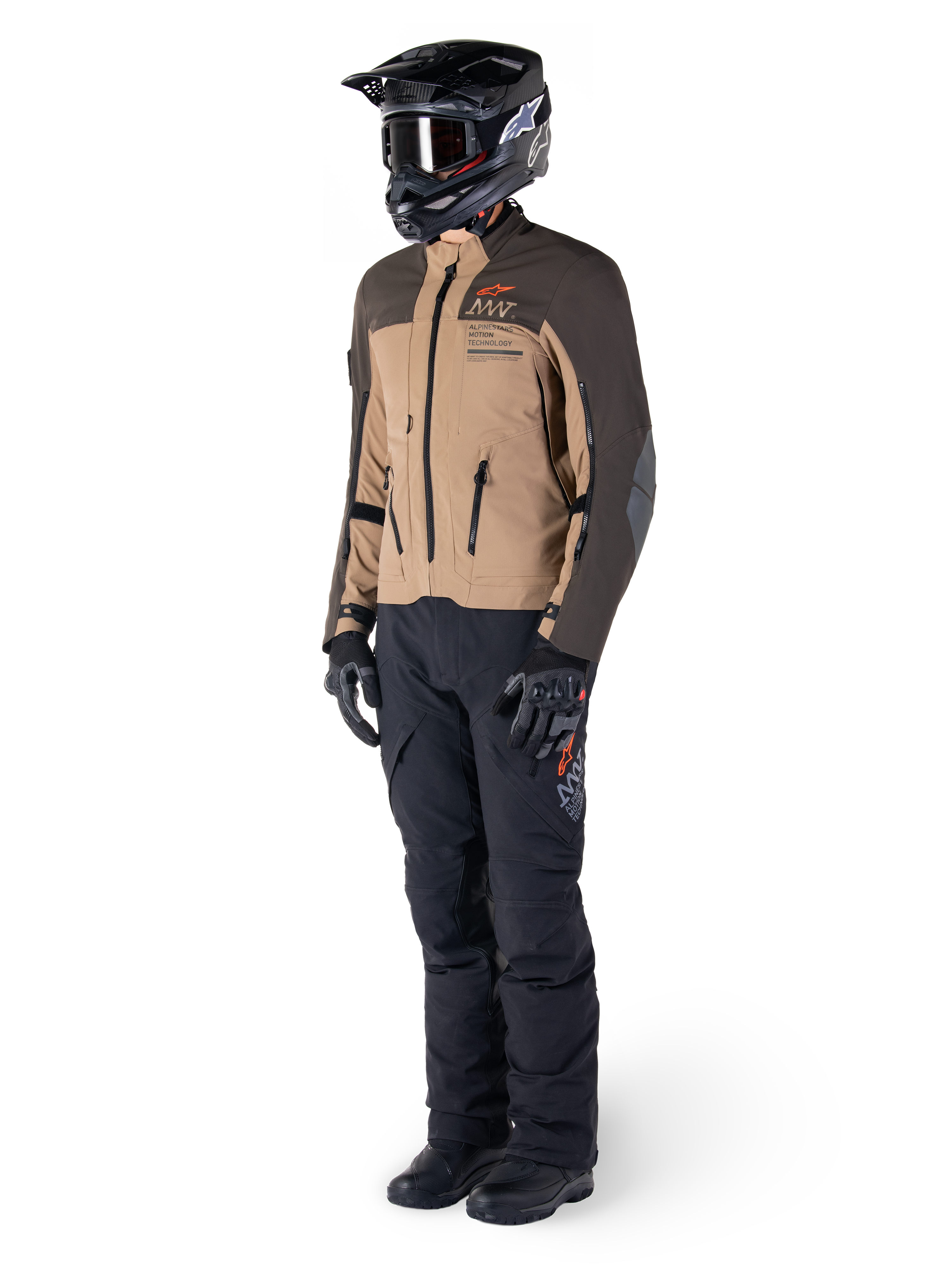 Pilote d'aventure portant un équipement complet, veste Alpinestars AMT-8 Stretch Drystar® XF en brun foncé et kaki foncé, associée à un pantalon d'aventure noir, un casque, des gants et des bottes noirs, avec logo AMT orange et fermetures éclair de ventilation techniques pour le touring longue distance.