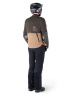 Veste Alpinestars AMT-8 Stretch Drystar® XF, veste de moto Adventure Touring, brun foncé et kaki foncé, vue arrière montrant le marquage 'AMT Alpinestars Motion Technology', portée avec un pantalon noir et un casque, design stretch ergonomique pour la conduite d'aventure