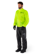 Man wearing Alpinestars Hurricane Rain V2 Jacket in Yellow Fluo and Hurricane Rain V2 Pants in Black, high-visibility waterproof motorcycle rain gear, featuring reflective logos on the chest and thigh, complete outfit with black gloves and boots.