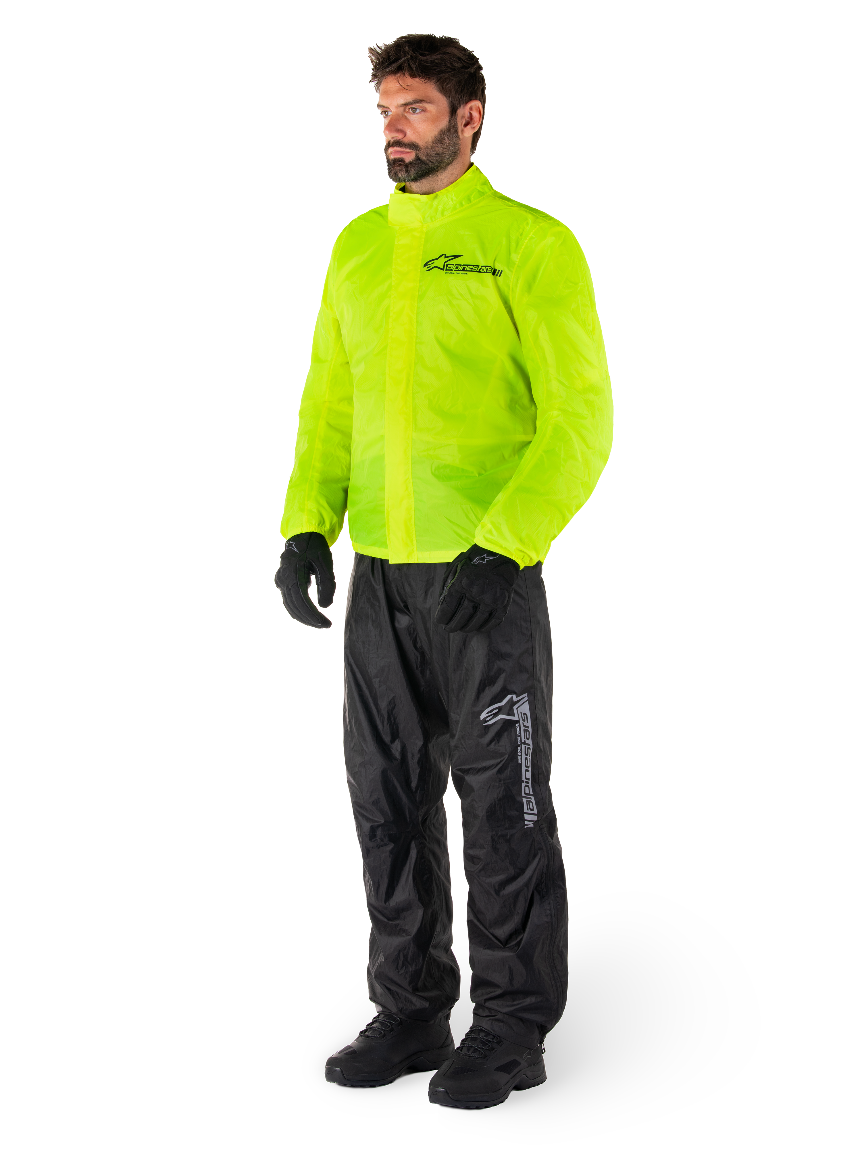 Man wearing Alpinestars Hurricane Rain V2 Jacket in Yellow Fluo and Hurricane Rain V2 Pants in Black, high-visibility waterproof motorcycle rain gear, featuring reflective logos on the chest and thigh, complete outfit with black gloves and boots.