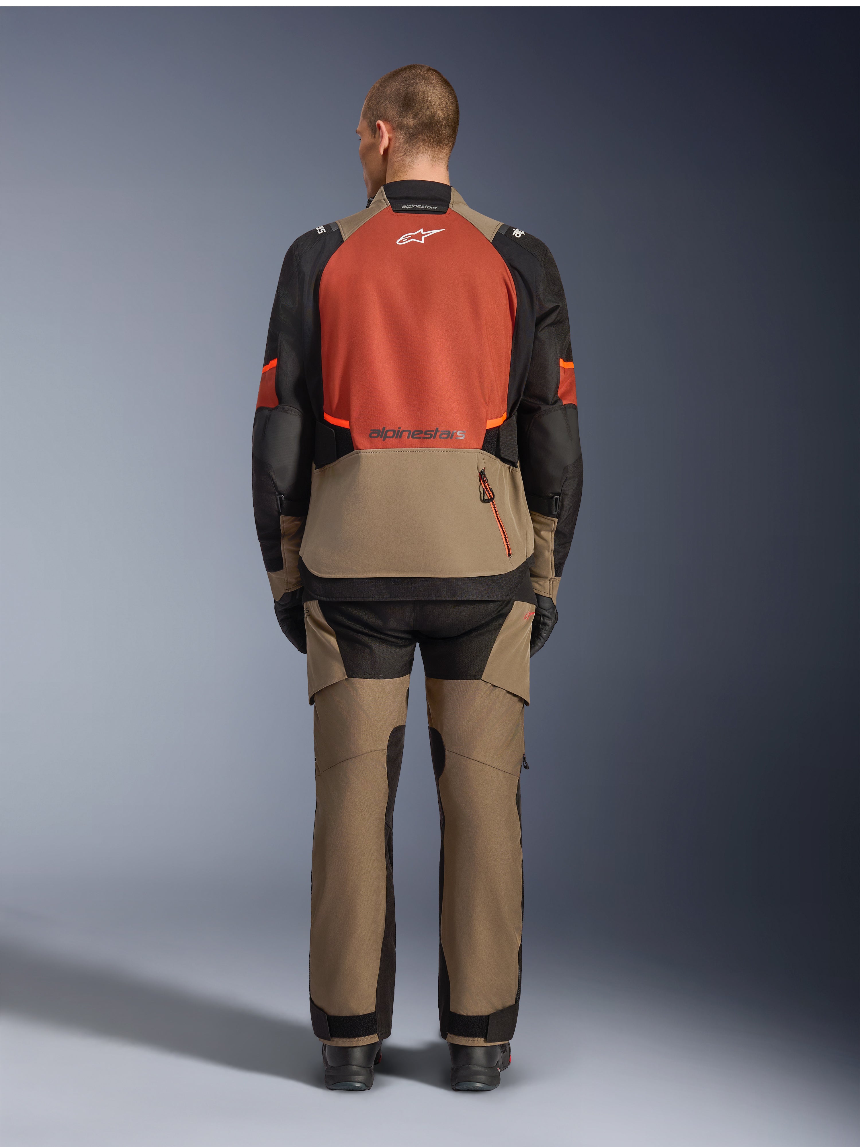 Veste Alpinestars Andes V4 Drystar®, Walnut Rust Black, vue arrière d'une veste de touring moto avec empiècement supérieur rouille et partie inférieure couleur noyer, portée avec un pantalon d'aventure assorti et des bottes noires