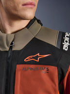 Veste Alpinestars Andes V4 Drystar® en Walnut Rust Black, gros plan sur le haut de la poitrine et l'épaule, avec logo A-star orange sur empiècement noir et marquage Alpinestars sur la section couleur rouille, détail d'équipement de moto d'aventure