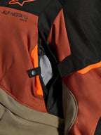 Veste Alpinestars Andes V4 Drystar®, Walnut Rust Black, gros plan sur l'ouverture de ventilation directe avec doublure en maille, textile durable avec accents orange, bouton-pression et détail du logo Alpinestars
