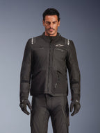 Mannequin masculin portant la veste Alpinestars Andes V4 Drystar® en noir, veste de moto d'aventure touring, avec pantalon et gants de moto noirs assortis, fermetures éclair imperméables et logo Alpinestars blanc sur la poitrine et les épaules, équipement de protection toutes saisons, prise de vue en studio