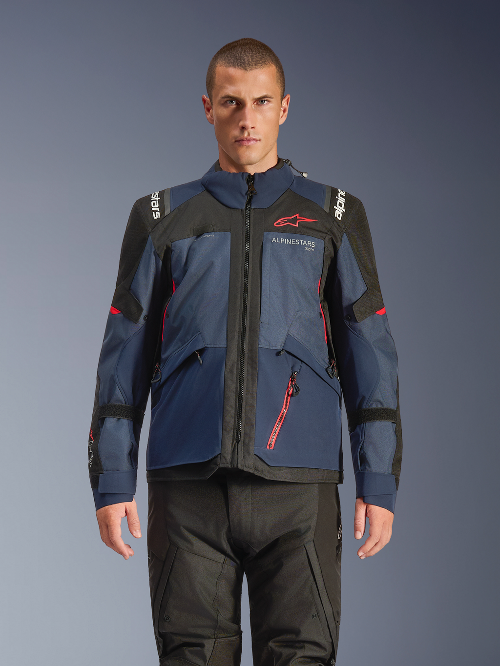 Veste Alpinestars Andes V4 Drystar®, veste de moto d'aventure, Night Navy et Mood Indigo avec empiècements noirs, portée par un mannequin avec un pantalon de moto noir, logo Alpinestars rouge sur la poitrine et détails de fermeture éclair rouges, construction textile durable pour le touring toutes saisons