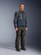 Modèle masculin portant la veste Alpinestars Andes V4 Drystar® en Night Navy et Mood Indigo avec empiècements noirs et accents rouges, associée à un pantalon de moto et des bottes noirs, équipement technique de touring d'aventure en studio.