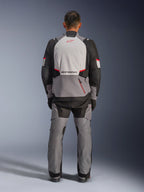 Veste Alpinestars Andes V4 Drystar®, veste de moto d'aventure, gris foncé, gris glacé, noir et rouge vif, vue arrière d'un pilote portant un pantalon assorti, avec un large panneau dorsal gris glacé et logo rouge, sections d'épaules renforcées noires et sangles de réglage à la taille pour le touring toutes saisons.