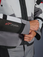 Détail de la manche de la veste Alpinestars Andes V4 Drystar®, textile gris et noir, logo Drystar rouge et blanc sur l'avant-bras, fermeture de poignet réglable par velcro, équipement de moto imperméable haute performance