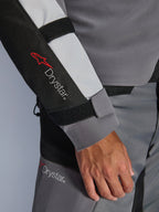 Gros plan sur la manche de la veste Alpinestars Andes V4 Drystar®, gris foncé et gris glace avec accents noirs, logo Drystar® et sangles de réglage à l'avant-bras, faisant partie d'une tenue de moto d'aventure imperméable en textile