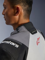 Veste Alpinestars Andes V4 Drystar®, gros plan sur le col et le haut du dos, gris foncé et gris glace avec détails noirs, logo étoile rouge, dotée d'un cordon de serrage au col et du marquage Alpinestars, construction textile durable