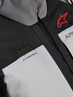 Veste Alpinestars Andes V4 Drystar®, gros plan sur la poitrine, panneaux gris foncé et gris glace avec renforts en textile noir, logo Alpinestars rouge et boucle pour tuyau d'hydratation avec étiquette 'HYDRATION'