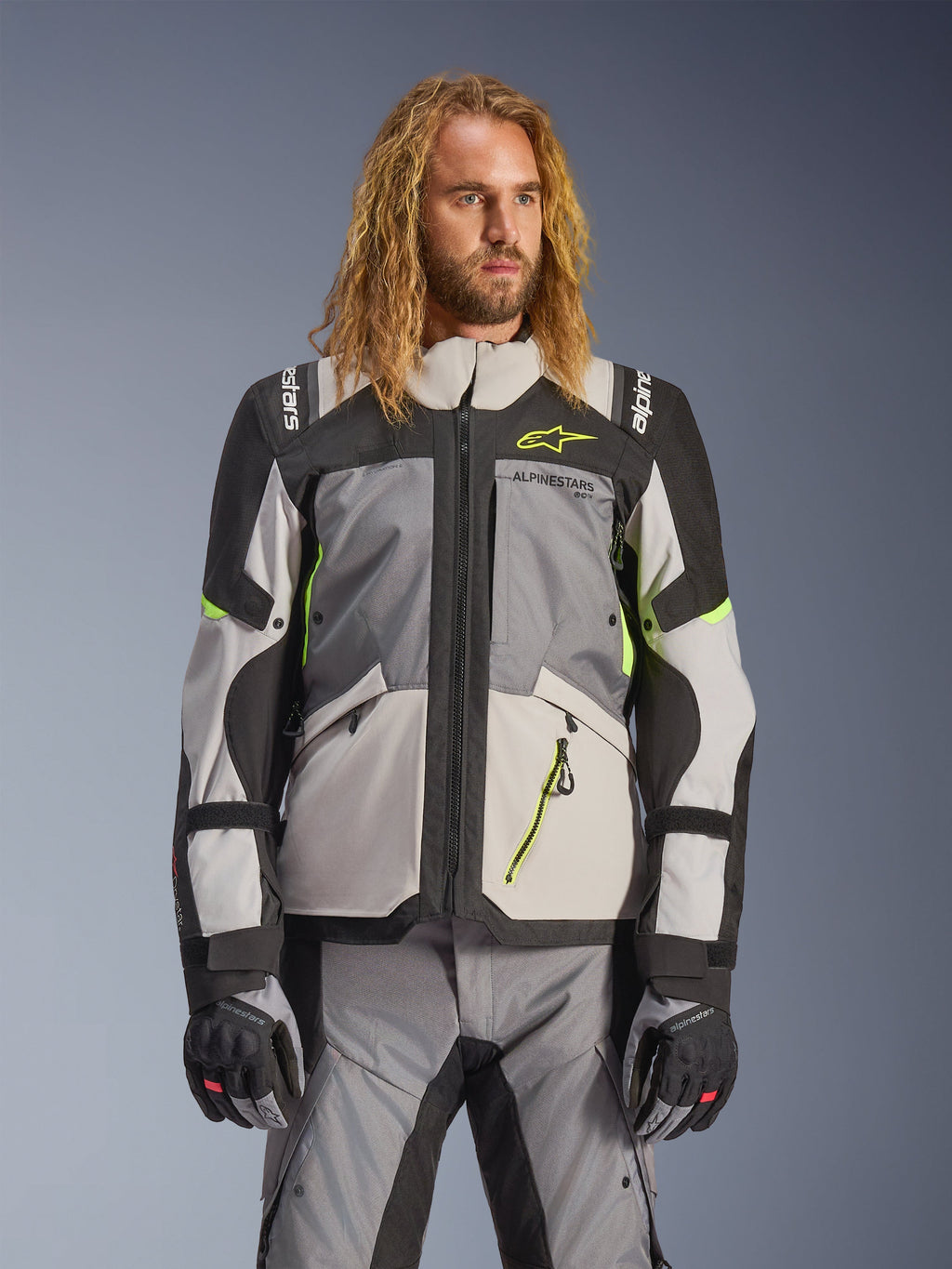 Alpinestars Andes V4 Drystar Jacket, Adventure Touring Motorcycle Jacket, Dark Gray and Ice Gray with Neon Yellow accents, worn by a model with matching pants and gloves, multi-pocket textile design for all-weather riding
