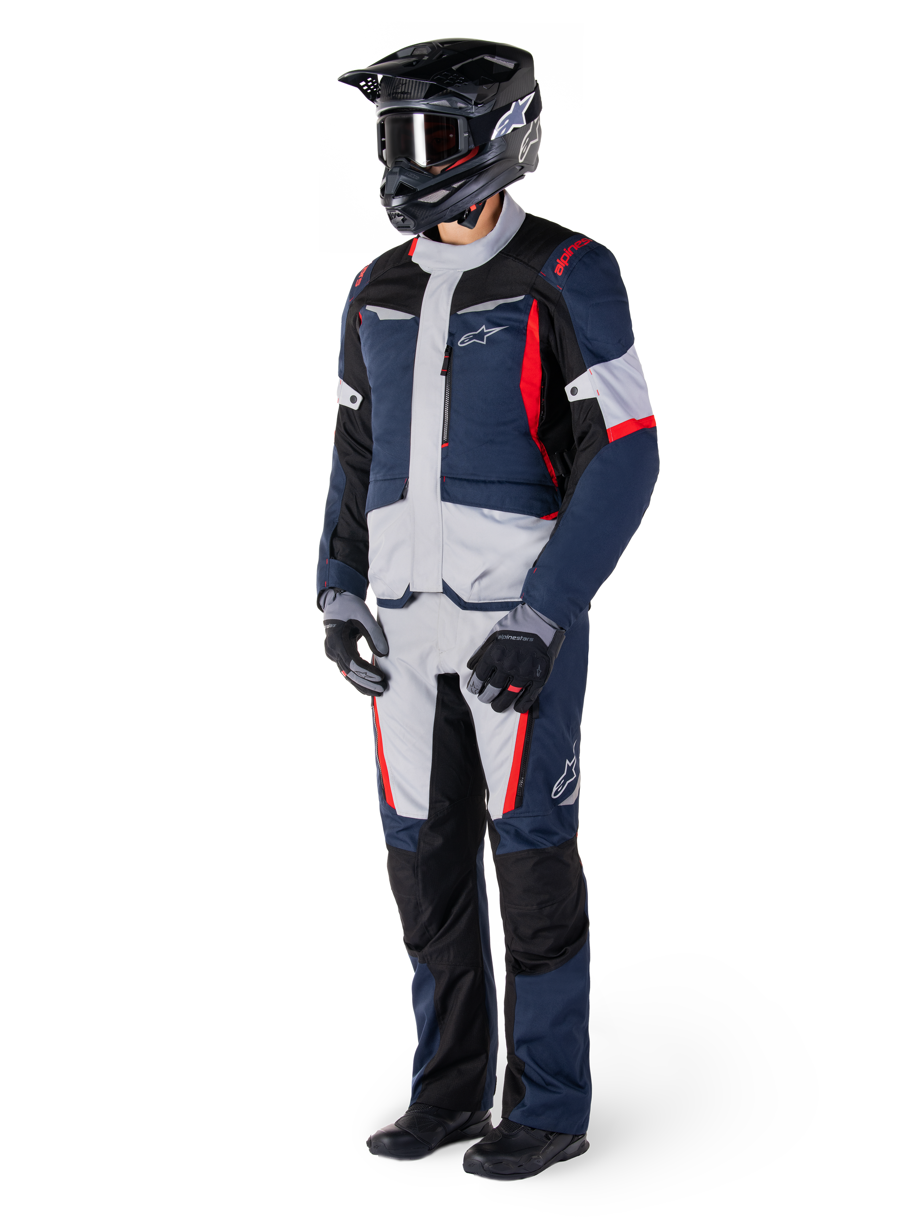 Veste Alpinestars ST-1 Waterproof, veste de tourisme d'aventure, bleu foncé, noir et rouge vif, portée par un motard avec pantalon assorti, casque d'aventure noir, gants et bottes, avec empiècements gris et touches de rouge, design épuré inspiré de l'aventure avec logos Alpinestars