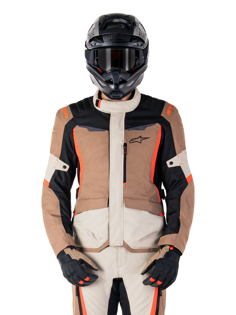 Veste imperméable Alpinestars ST-1, Dark Khaki Sand Black Red Fluo, portée par un pilote avec un casque et des gants noirs, équipement de touring aventure avec empiècements beige et marron et accents rouge fluo vifs, vue de face sur fond blanc.