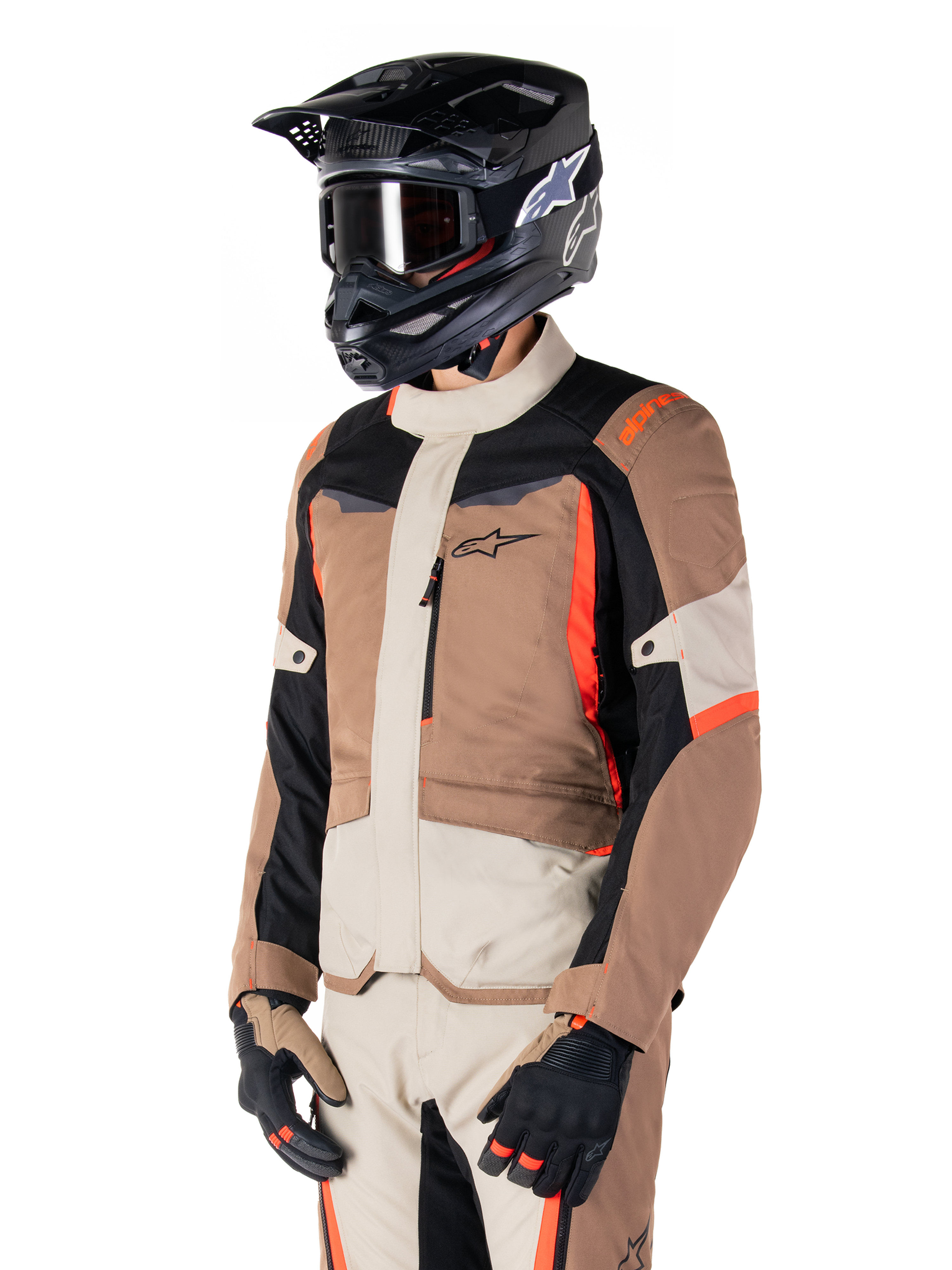 Veste imperméable Alpinestars ST-1, veste de touring aventure, kaki foncé, sable, noir et rouge fluo, portée par un motard avec un casque de motocross noir et des lunettes, dotée d'une conception multi-panneaux avec des poches cargo et le logo Alpinestars sur la poitrine