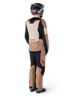 Veste imperméable Alpinestars ST-1, veste de touring aventure, kaki foncé, sable, noir et rouge fluo, vue arrière portée avec un pantalon assorti et un casque noir, avec des panneaux color-block et des accents rouges fluorescents.