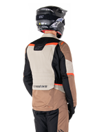 Veste imperméable Alpinestars ST-1, veste d'aventure touring, Dark Khaki Sand Black Red Fluo, vue arrière montrant des empiècements textiles color-block, des accents rouge fluo et le marquage Alpinestars dans le bas du dos, portée par un motard avec un casque noir.