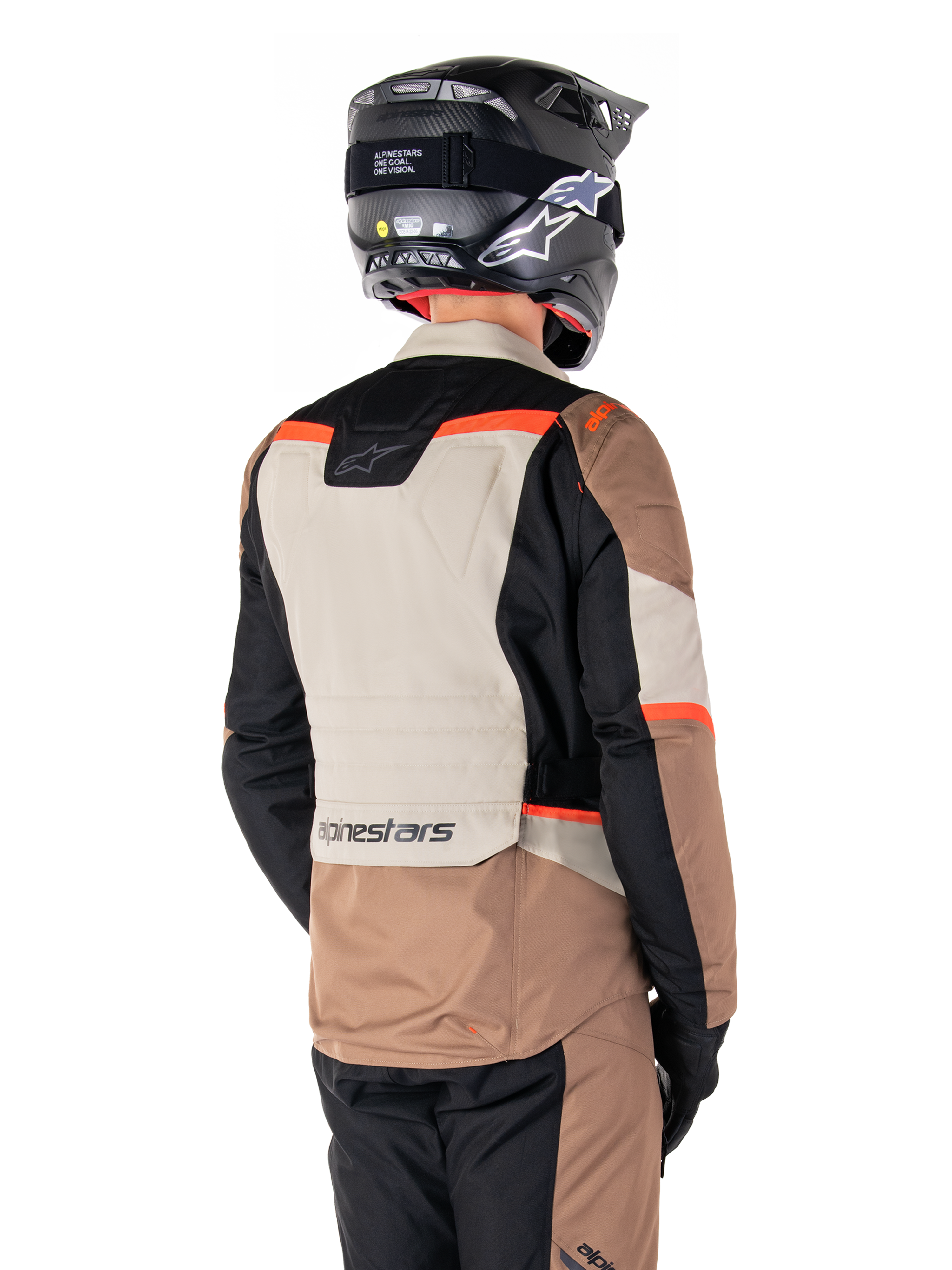 Veste imperméable Alpinestars ST-1, veste d'aventure touring, Dark Khaki Sand Black Red Fluo, vue arrière montrant des empiècements textiles color-block, des accents rouge fluo et le marquage Alpinestars dans le bas du dos, portée par un motard avec un casque noir.