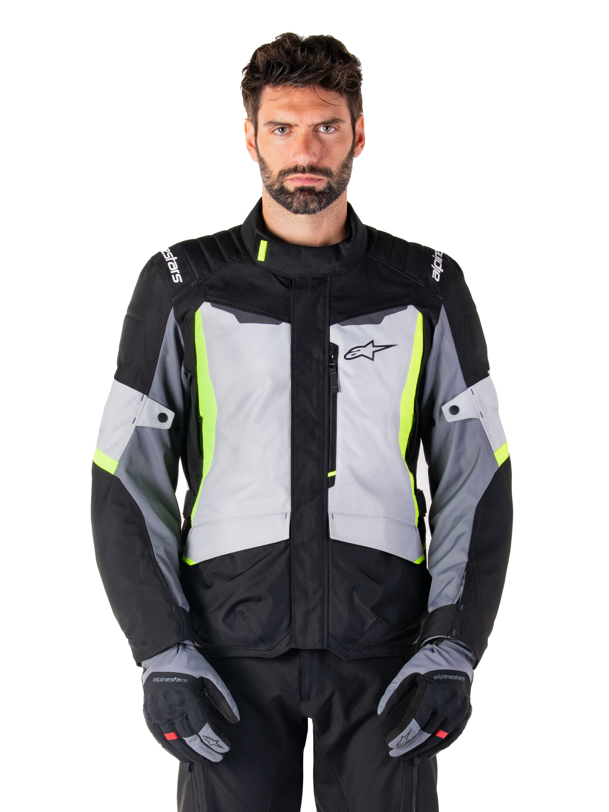 Veste imperméable Alpinestars ST-1, veste de moto adventure touring, Gris Glacé, Noir et Jaune Fluo, portée par un homme avec des gants assortis et un pantalon noir, dotée de détails jaune fluo sur la poitrine et le col, logo Alpinestars sur la poitrine