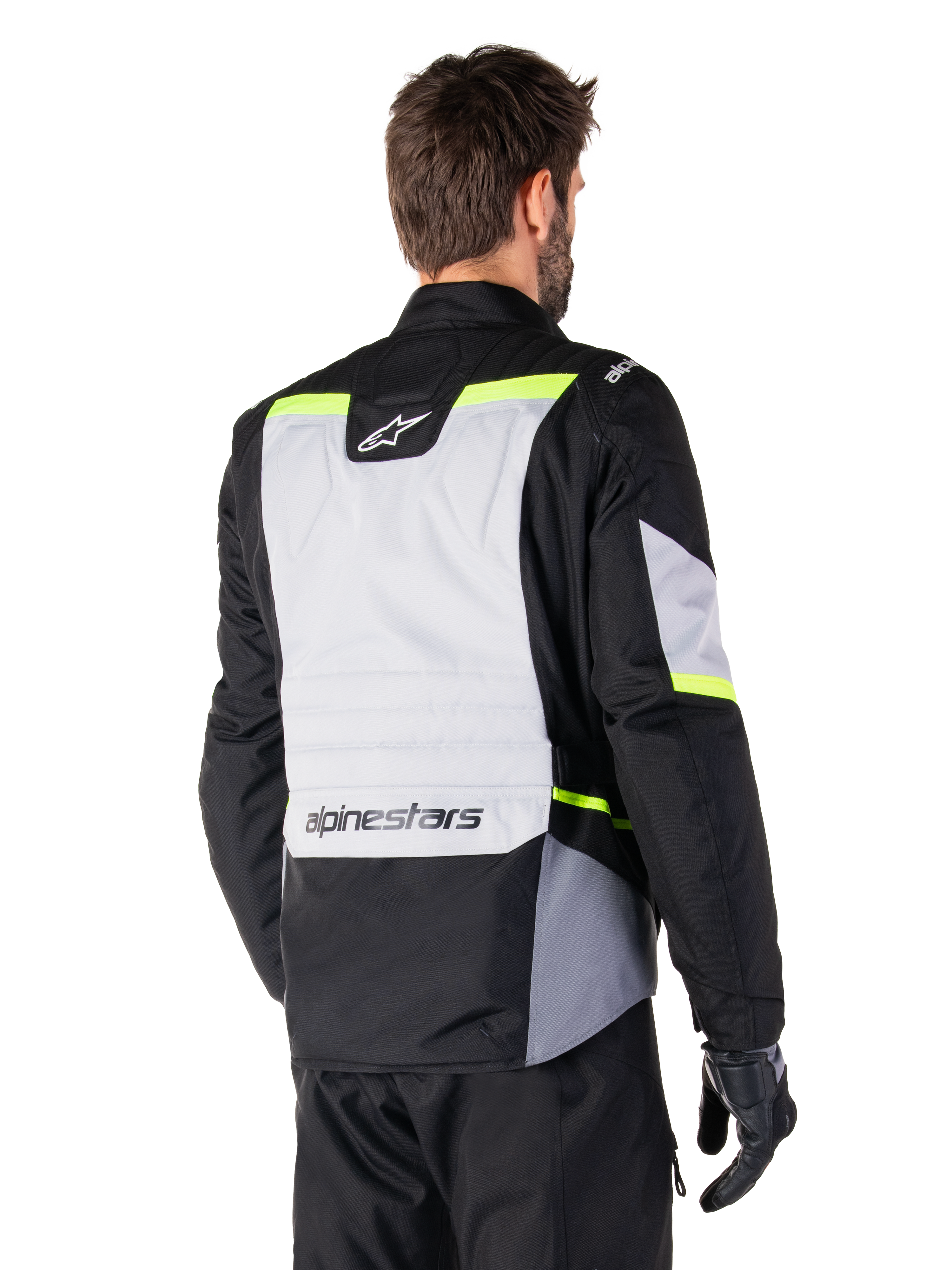 Alpinestars ST-1 Waterproof Jacket in Ice Gray Black Yellow Fluo, rear three-quarter view of a rider wearing the adventure touring jacket, featuring a large gray back panel with fluorescent yellow accents and Alpinestars branding, paired with black riding pants and gloves