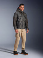 Modèle masculin portant la veste Alpinestars Mospher Waterproof noire, parka imperméable d'inspiration utilitaire avec design multi-poches et capuche, associée à un pantalon cargo beige et des baskets montantes noires, équipement de moto urbain.
