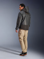Homme portant la veste imperméable Alpinestars Mospher en noir, vue de profil arrière et latéral, avec pantalon cargo beige et baskets noires, design parka à capuche en tissu ripstop, marquage Alpinestars sur la manche, style moto urbain moderne