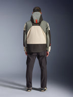 Vue de dos d'un motard portant la veste imperméable Alpinestars Mospher en Fur Gray Black Ice, parka d'inspiration tactique avec design color-block gris, noir et crème, dotée d'une capuche avec sangle orange, associée à un pantalon cargo noir.