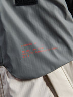 Veste imperméable Alpinestars Mospher, parka de moto, Fur Gray et Black Ice, détail du tissu technique ripstop avec marquage et slogan Alpinestars rouges, mettant en avant une construction durable et un design tactique urbain