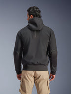 Veste imperméable Alpinestars Moblast, noire, vue arrière d'une veste de moto urbaine à capuche, avec logo « astars » vertical au dos, taille et poignets élastiqués, coudes renforcés et design technique moderne, portée avec un pantalon cargo beige