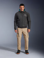 Veste imperméable Alpinestars Moblast, hoodie de moto urbain noir avec doublure de capuche bleu sarcelle, porté avec un pantalon cargo beige et des bottes montantes noires, vêtement de moto contemporain toutes saisons