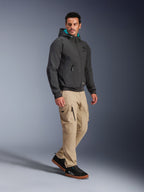 Mannequin homme portant la veste imperméable Alpinestars Moblast en noir, hoodie de moto urbain avec capuche doublée de bleu sarcelle, associé à un pantalon cargo kaki et des baskets noires, design minimaliste moderne avec tissu technique extensible pour les trajets par tous les temps