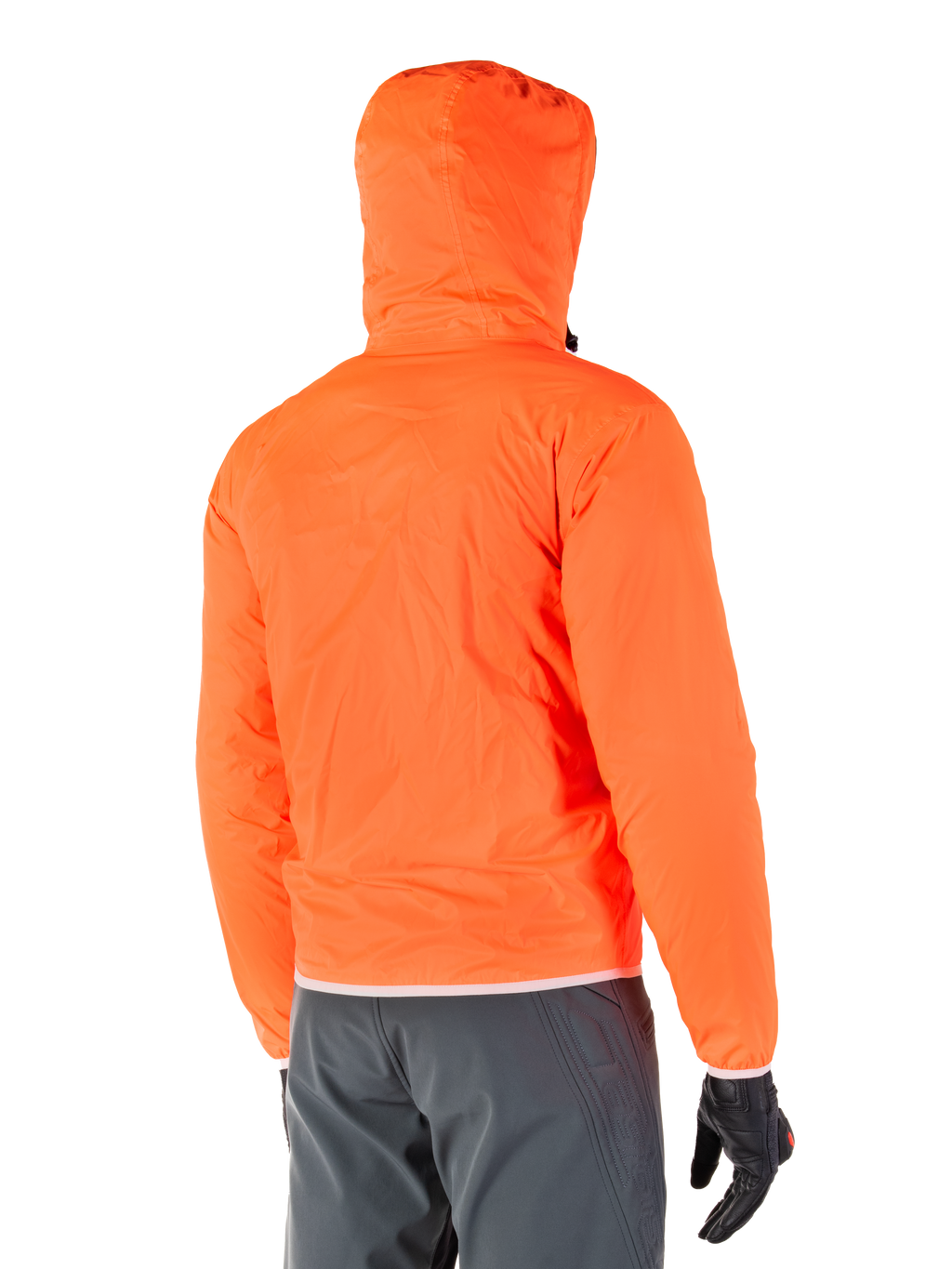 Veste Mohobbs Waterproof d'Alpinestars, doublure de pluie d'urgence compressible de couleur orange fluo éclatant, vue arrière montrant la capuche anti-tempête, portée avec un pantalon de moto gris foncé et des gants noirs, équipement de moto urbain léger et imperméable