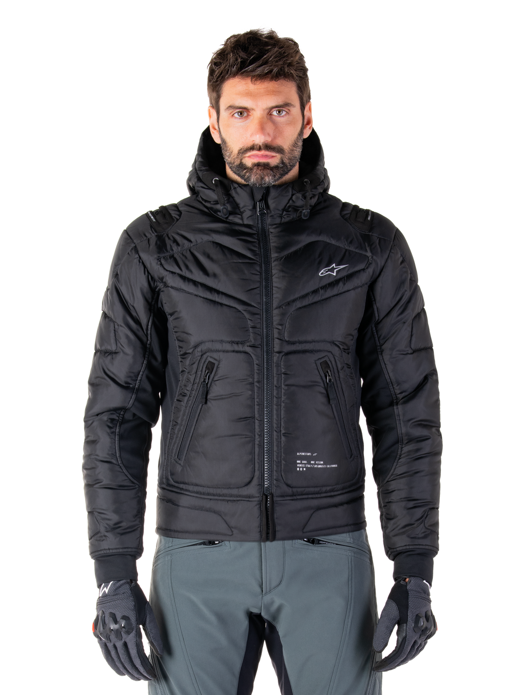 Veste Alpinestars Mohobbs Waterproof, blouson aviateur de moto rembourré noir, tissu poly matelassé avec fermeture éclair centrale et poches zippées, petit logo blanc sur la poitrine, porté par un mannequin avec un pantalon gris et des gants, design streetwear urbain pour la conduite en ville.